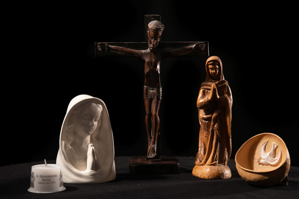 Föremål som hänger samman med den katolska kyrkan; ett ljus, ett krucifix, två Maria statyer och en vigvattenskål.